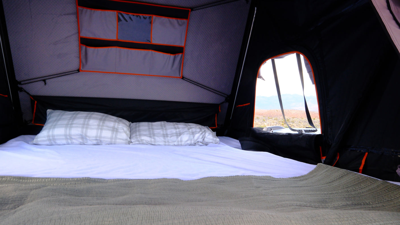 RV rental interior: A cozy rooftop tent bed with pillows & blanket, offering a stunning desert landscape view from the window.