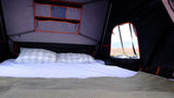 RV rental interior: A cozy rooftop tent bed with pillows & blanket, offering a stunning desert landscape view from the window.