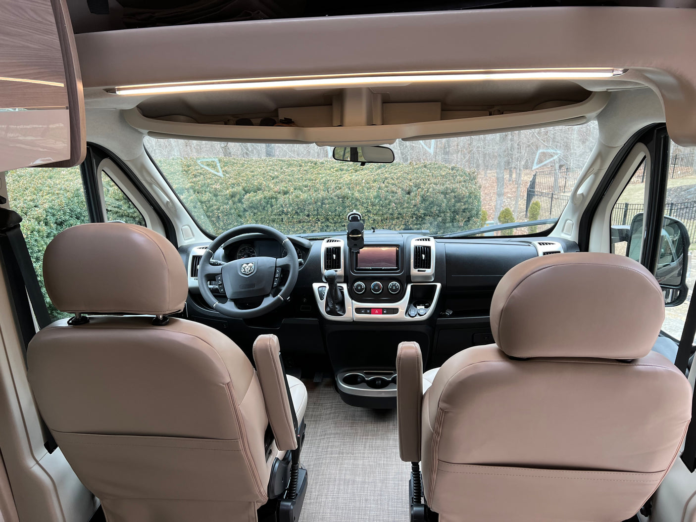 RV rental: Inside view of the front cabin with driver's dashboard, steering wheel, and light tan captain's seats.