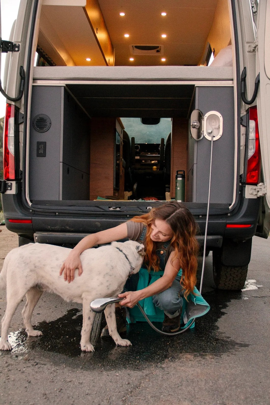  enjoying scenic mountain views from her camper van bed.|Cozy rv rental: A person on the bed and a dog below enjoy the sunset view from their camper van.|RV rental kitchen: A compact two-burner gas stove sits in a sunlit bamboo countertop — photo 12