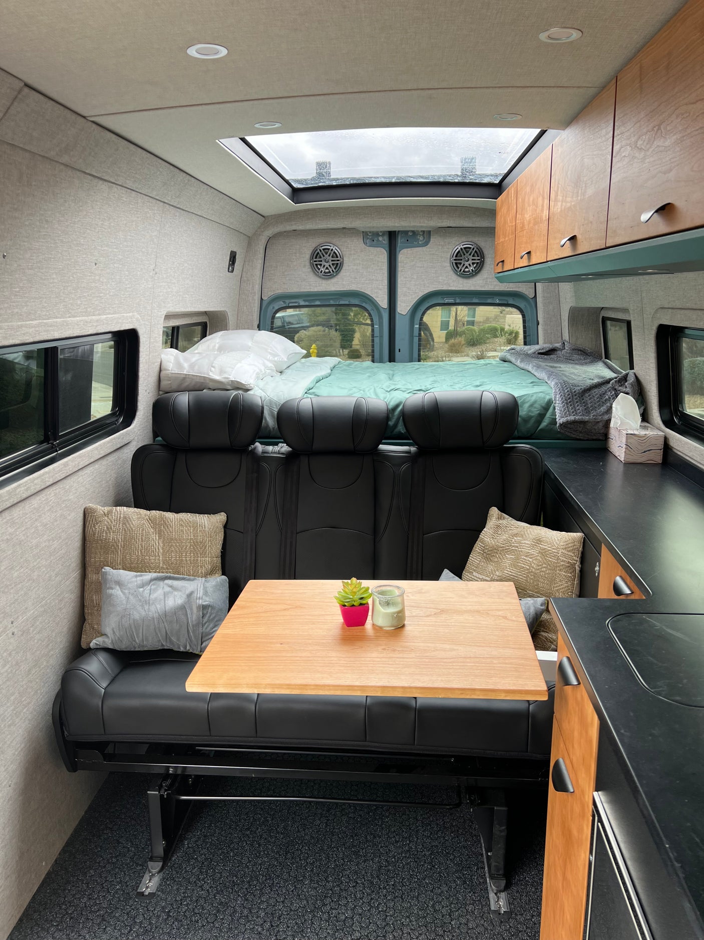 Inside a comfortable RV rental: dining area with wooden table, plush seating, and rear bed for a complete mobile living space.