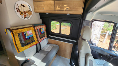 Inside a comfy RV rental: light bench seating, wood cabinets, & window view of nature.