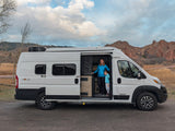 Woman & child in their white Solis RV rental van, parked near scenic red rock formations.