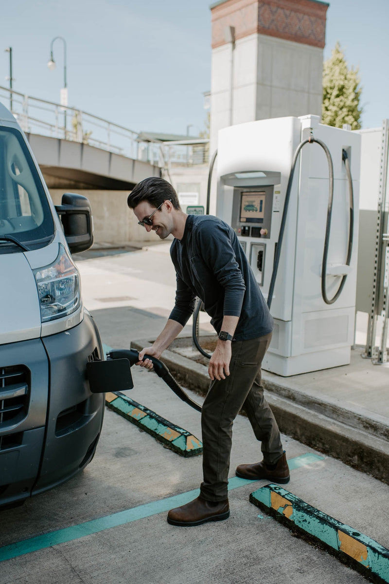 Smiling man plugs his electric RV rental into an EV charging station. Outdoor scene with a large white van. — photo 12
