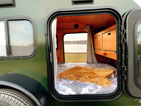 Step into this cozy RV rental camper with a comfortable bed and stunning lakeside view, perfect for a nature escape.