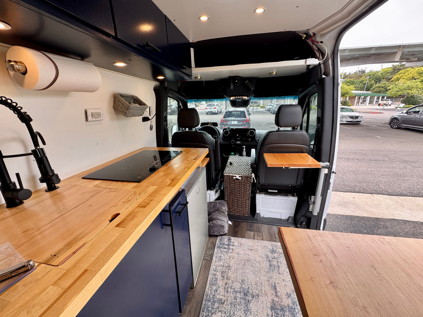 RV rental: Camper van interior with wood kitchen counter, induction cooktop, sink, and front seats.
