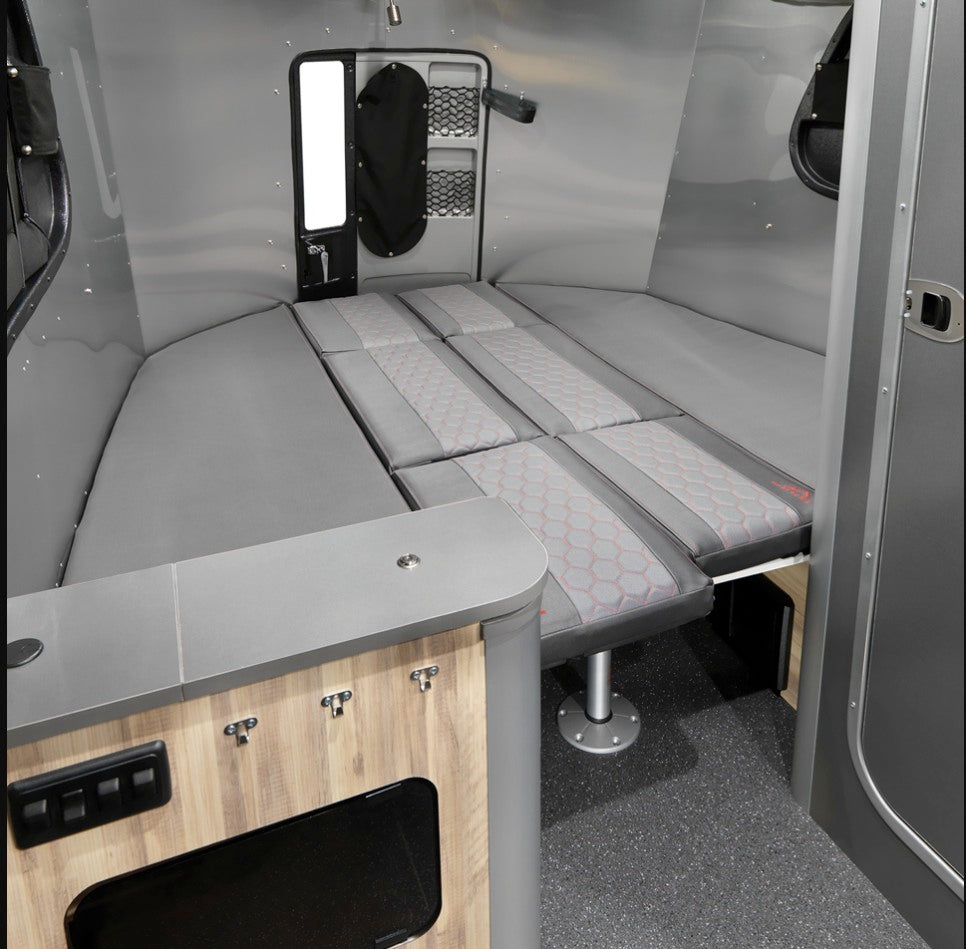 Compact RV rental: versatile interior with a full-size convertible bed, patterned cushions, and a small built-in counter.