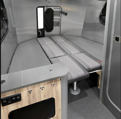 Compact RV rental: versatile interior with a full-size convertible bed, patterned cushions, and a small built-in counter.