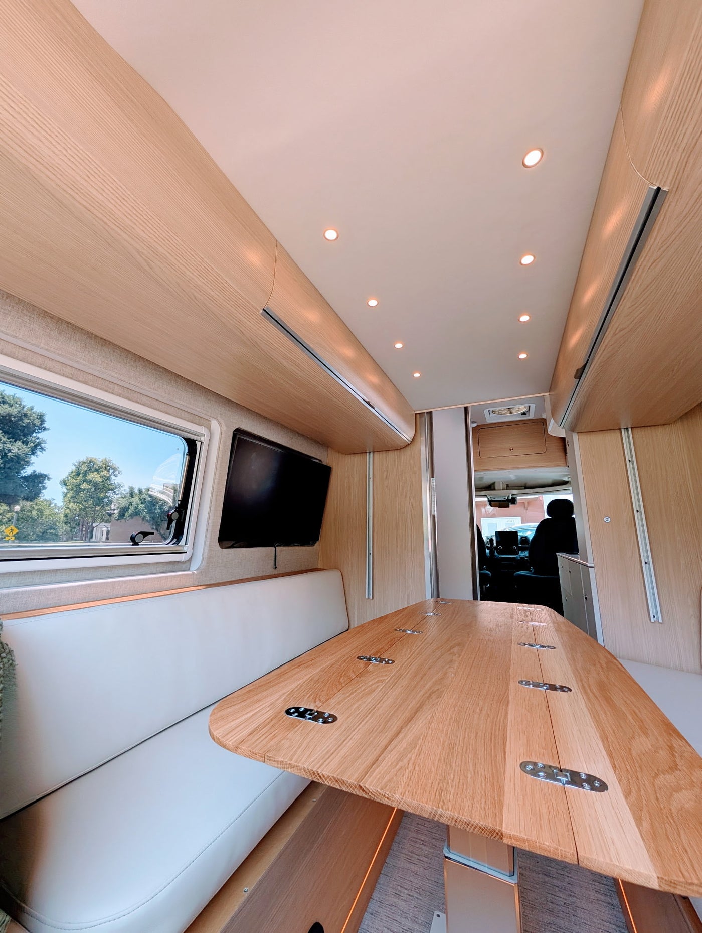 Bright, modern rv rental interior with a light wood dinette table, comfy white seating, TV, and recessed ceiling lights. — photo 4
