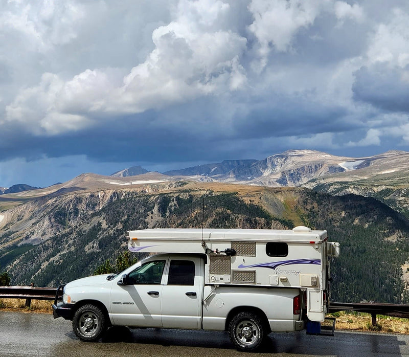 " parked with deployable steps and external AC. Ideal for an rv rental.|A white Northstar RV rental truck camper overlooks a vast mountain range under a cloudy sky.|This white Northstar truck camper — photo 6