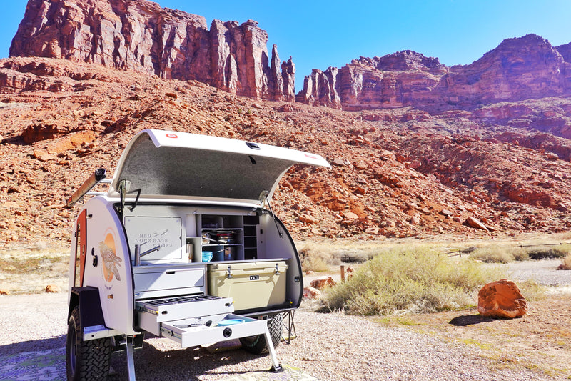 Open RV rental teardrop trailer showing its outdoor kitchen with a Yeti cooler, parked in a scenic red rock desert campsite. — photo 13