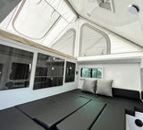 Inside a modern RV rental: a bright pop-up roof, black padded seating that converts to a bed, and wall storage.