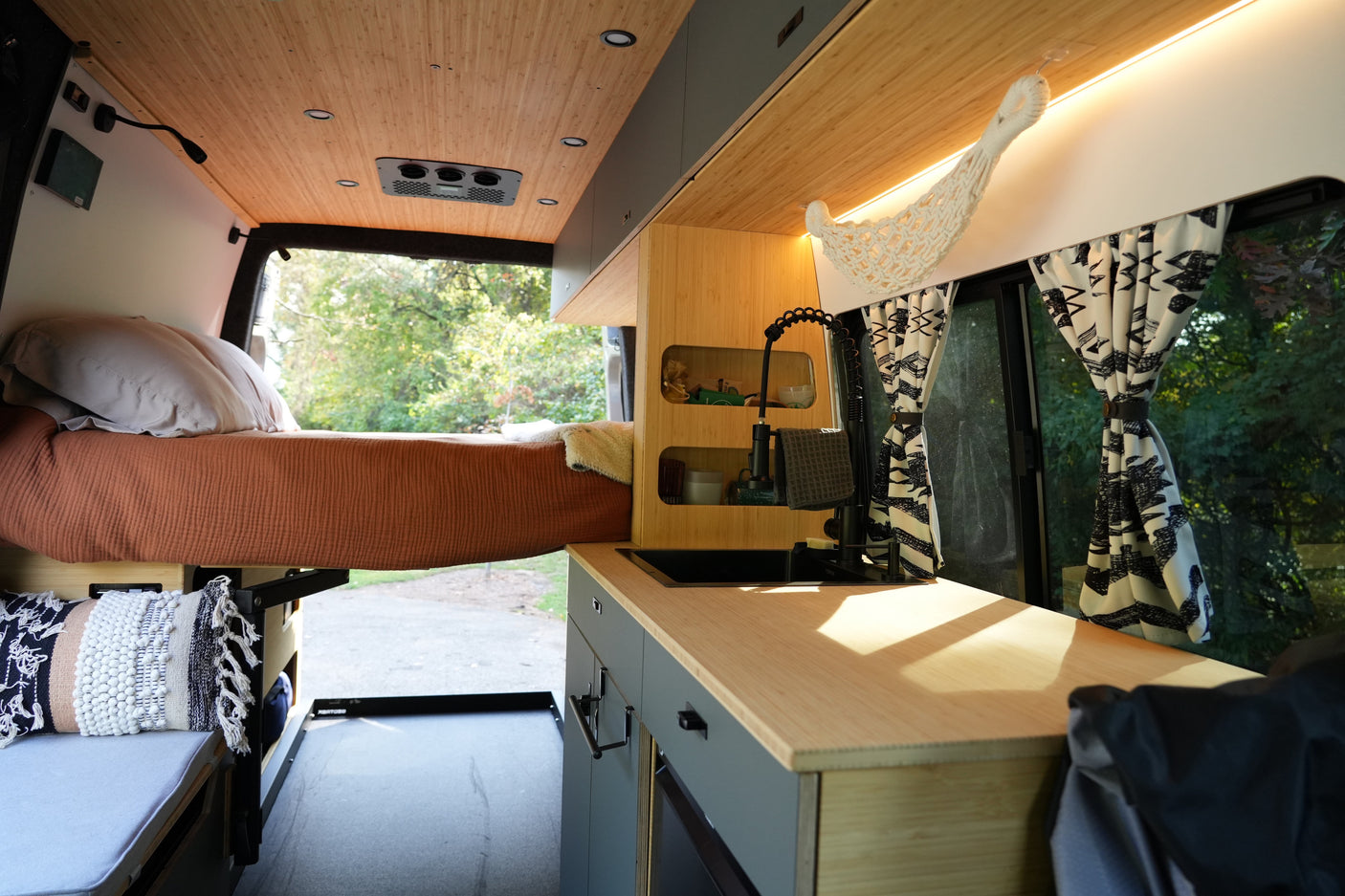 Modern RV rental interior showcasing a compact bed, stylish kitchenette, and warm bamboo paneling with window views.