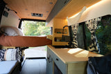 Modern RV rental interior showcasing a compact bed, stylish kitchenette, and warm bamboo paneling with window views.