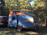A blue Cricket pop-up camper attached to an SUV in a sunny pine forest, perfect for an rv rental adventure.
