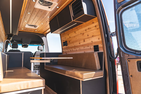 Inside an RV rental: wood-paneled interior with built-in seating, storage, and a movable table for comfortable travel.