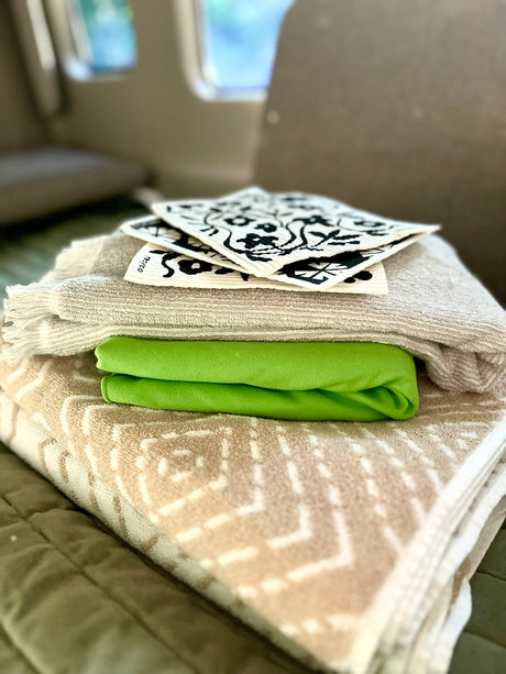 RV rental essentials: neatly stacked towels, green fabric, and eco-friendly patterned cleaning cloths for travel.