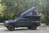 This rugged green Toyota Tacoma features a pop-up rooftop tent and bed camper, perfect for an RV rental wilderness trip.