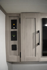 RV rental interior: Wall-mounted power outlet, USB, & coaxial cable hookups on light wood cabinetry.