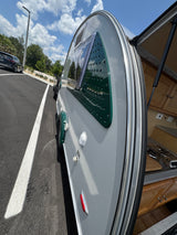 Explore with this stylish gray and green teardrop RV rental! Rear hatch open reveals compact kitchen; parked on asphalt.
