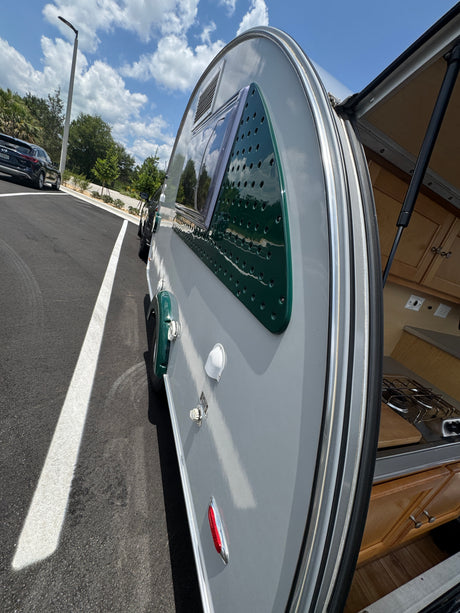 Explore with this stylish gray and green teardrop RV rental! Rear hatch open reveals compact kitchen; parked on asphalt.