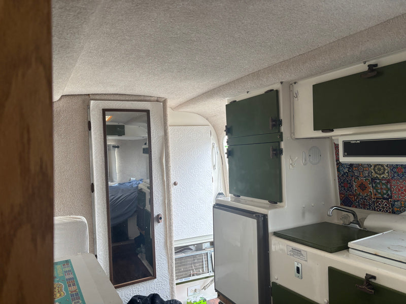 RV rental interior: a compact kitchenette with green cabinets, sink, fridge, and a mirrored door reflecting the sleeping area. — photo 6