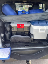 RV rental's cargo area neatly packed with camping gear: cooler, blue duffel bags, water jug, and storage cases.
