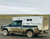 A robust, mud-splattered pickup truck with a mounted Bronco truck camper. Ideal for an adventurous RV rental exploring remote landscapes.