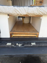 Efficient under-bed storage in an RV rental camper van, featuring a wooden pull-out tray on glides. Ideal for organized travel.