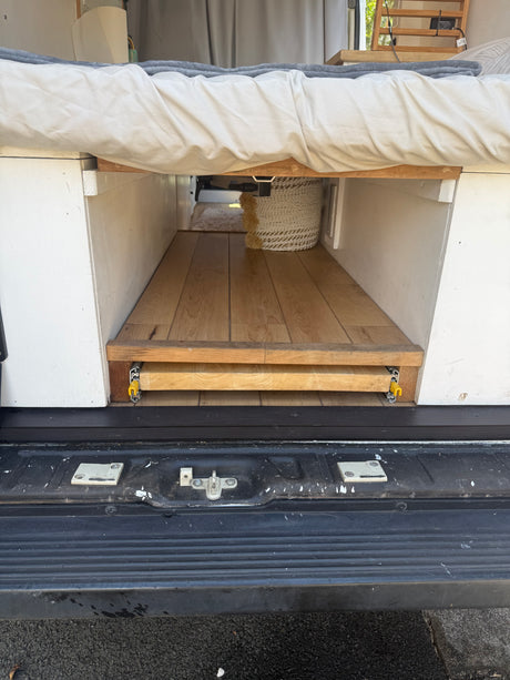 Efficient under-bed storage in an RV rental camper van, featuring a wooden pull-out tray on glides. Ideal for organized travel.