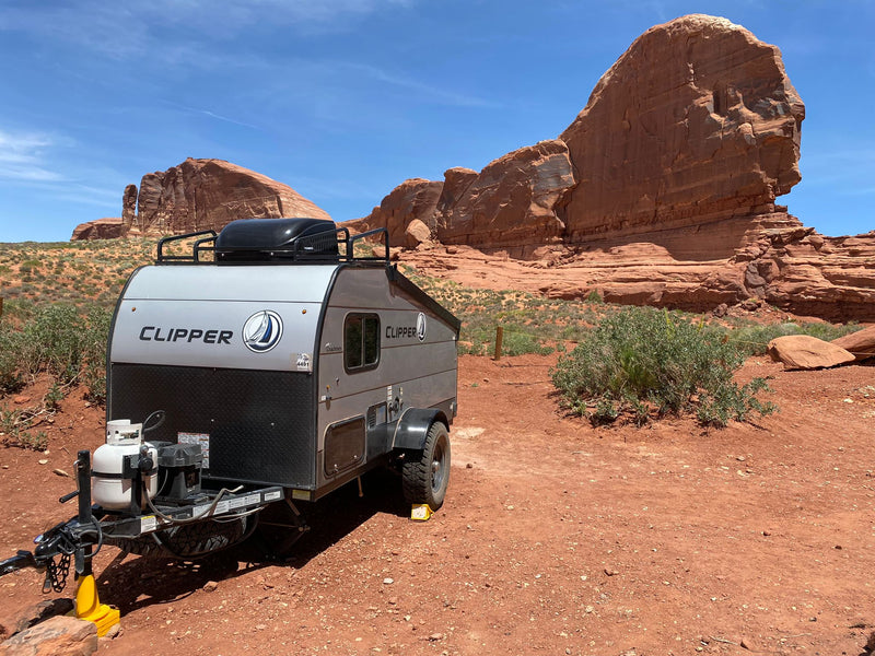 Small silver Clipper travel trailer (rv rental) on red dirt with striking red rock mountains under a blue sky. Ideal for outdoor adventure.|A rugged Coachmen Clipper travel trailer — photo 1