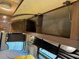 Inside an rv rental: open overhead storage cabinets with gas struts. A smoke detector and rolled-up window insulation are visible.