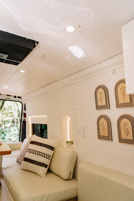 Bright RV rental living space featuring cream seating, wooden floral decor, recessed lighting, and a nature view.