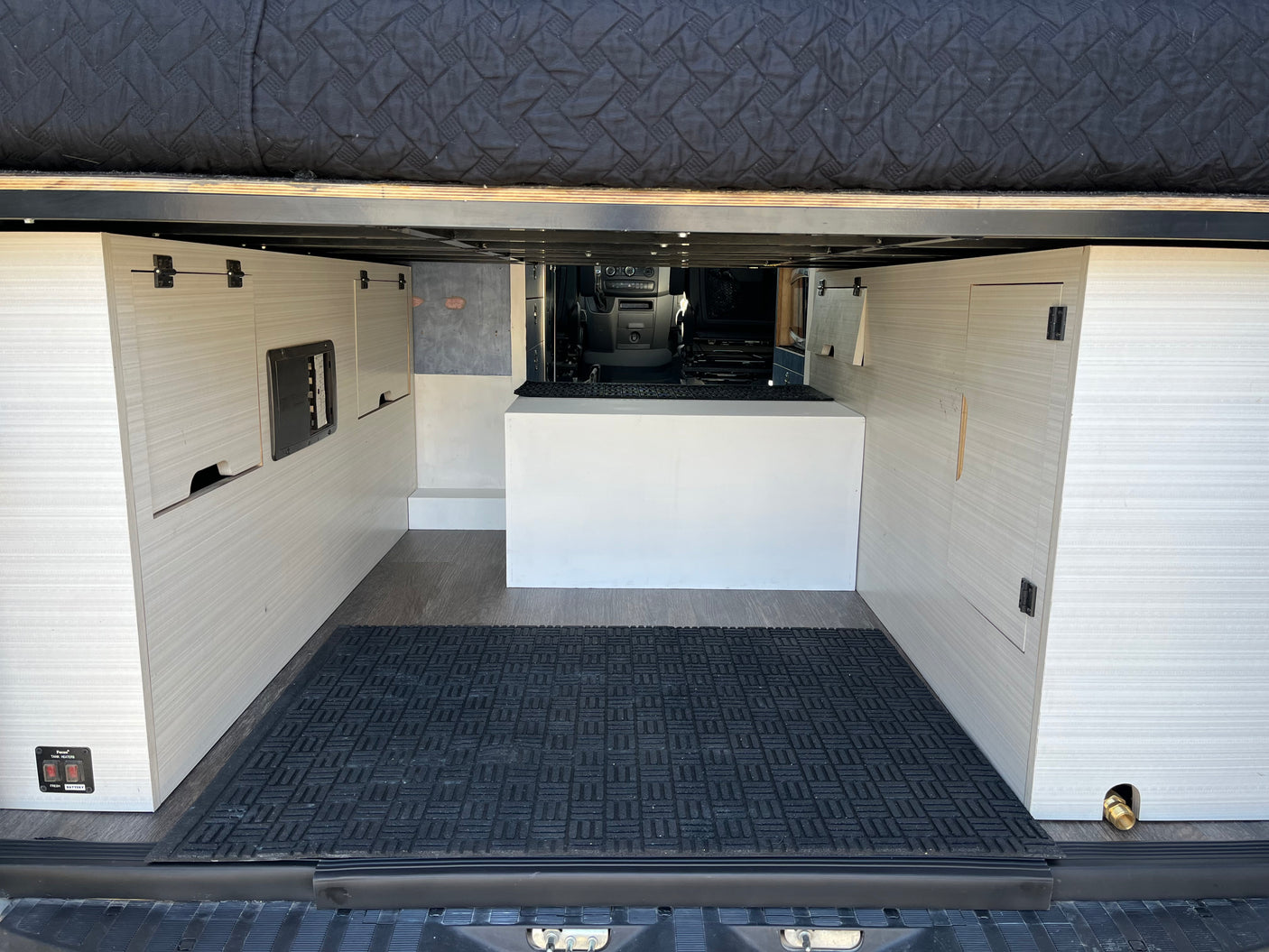 Inside this rv rental, a versatile rear storage area features a raised bed platform, side cabinets, utility controls, and durable flooring.
