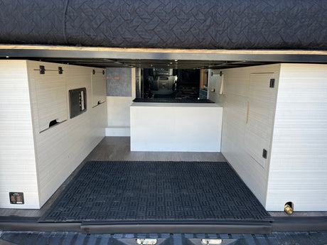 Inside this rv rental, a versatile rear storage area features a raised bed platform, side cabinets, utility controls, and durable flooring.