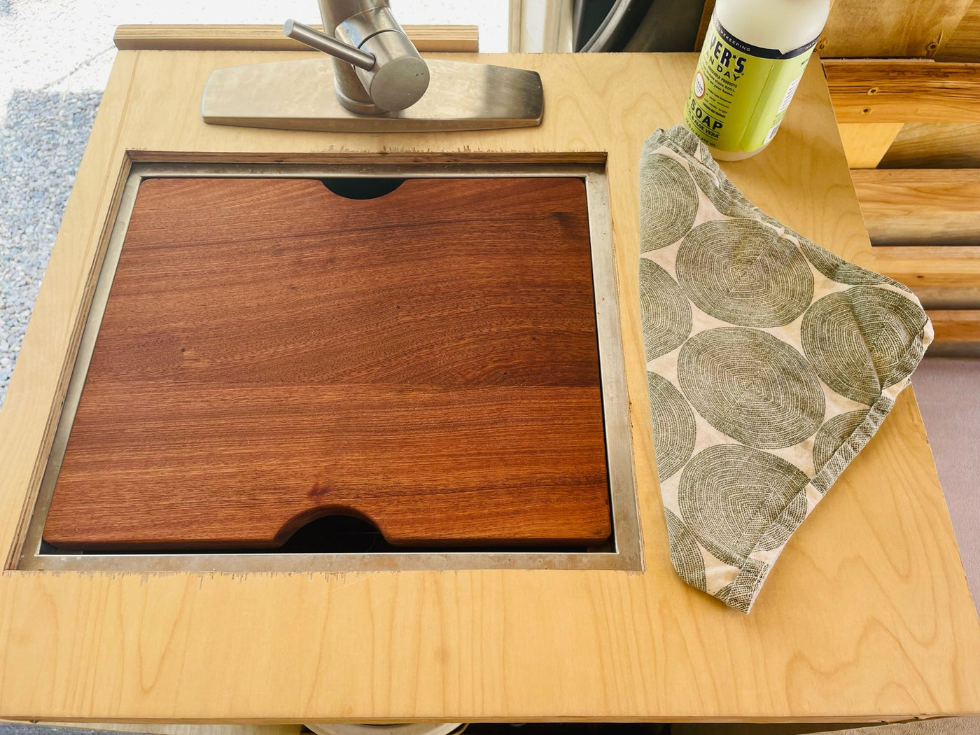 This RV rental features a compact kitchen with a covered sink/cutting board, faucet, soap, and dishtowel for efficient space. — photo 5