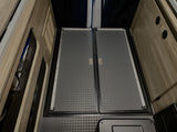 RV rental: Inside view of camper van floor with modular panels, L-track, storage nets & wood cabinets.