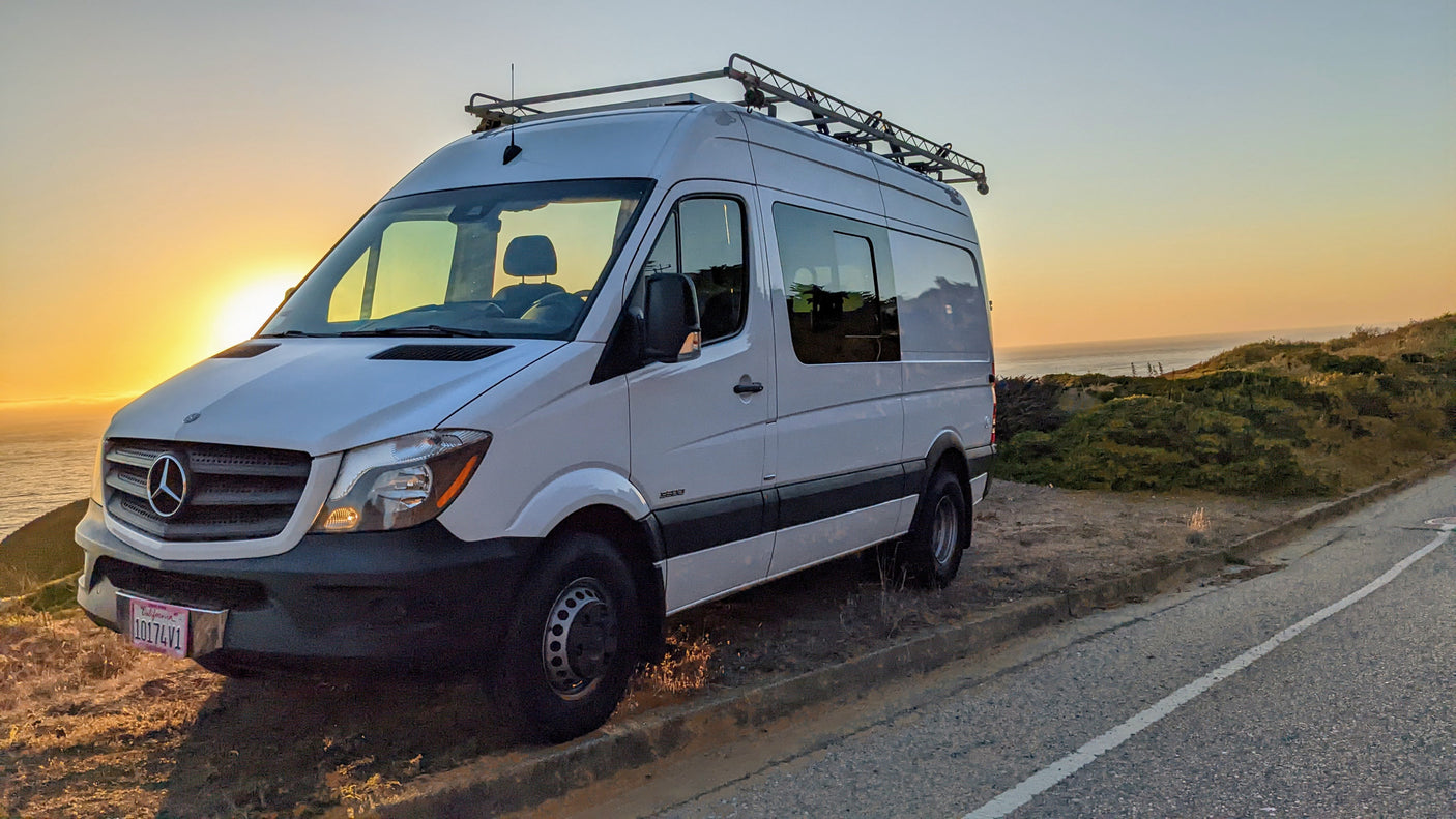White Mercedes Sprinter RV rental parked at sunset overlooking the ocean, ready for a scenic coastal road trip.