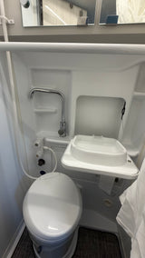 Compact RV rental bathroom showcasing a toilet, fold-down sink, and multi-use shower faucet for efficient travel.