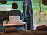 RV rental mobile office: Laptop & plant on table with wooded campsite view. Ideal for remote work/van life.