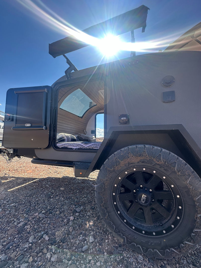 Adventure-ready RV rental trailer on gravel. Open door reveals a cozy, wood-paneled interior for off-road camping. — photo 9