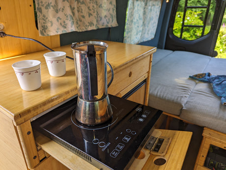 Enjoying coffee in a mobile kitchen setup inside an RV rental. Moka pot on an induction cooktop with cups on a bamboo counter.