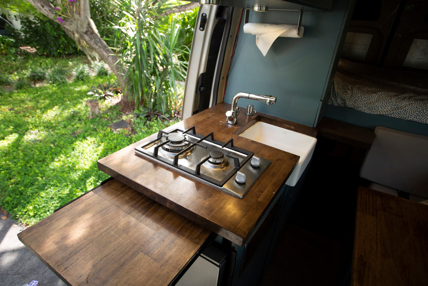 Modern RV rental kitchen with a gas stove, sink, and wood counters, overlooking a vibrant green garden. — photo 4