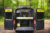 This RV rental camper van is open, revealing its customized interior with a bed & storage, ready for forest adventures.