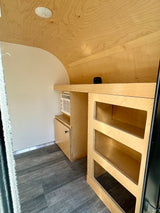 Modern RV rental interior: light wood cabinetry, AC unit, and open shelves optimize space in this compact camper.