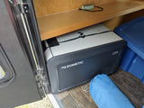An RV rental interior shows a Dometic CFX portable fridge on wood-look flooring, with a blue tote and shelf.