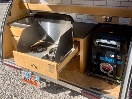 Explore this RV rental's teardrop trailer kitchen, featuring a pull-out stove, sink, and fridge, ideal for mobile camping.