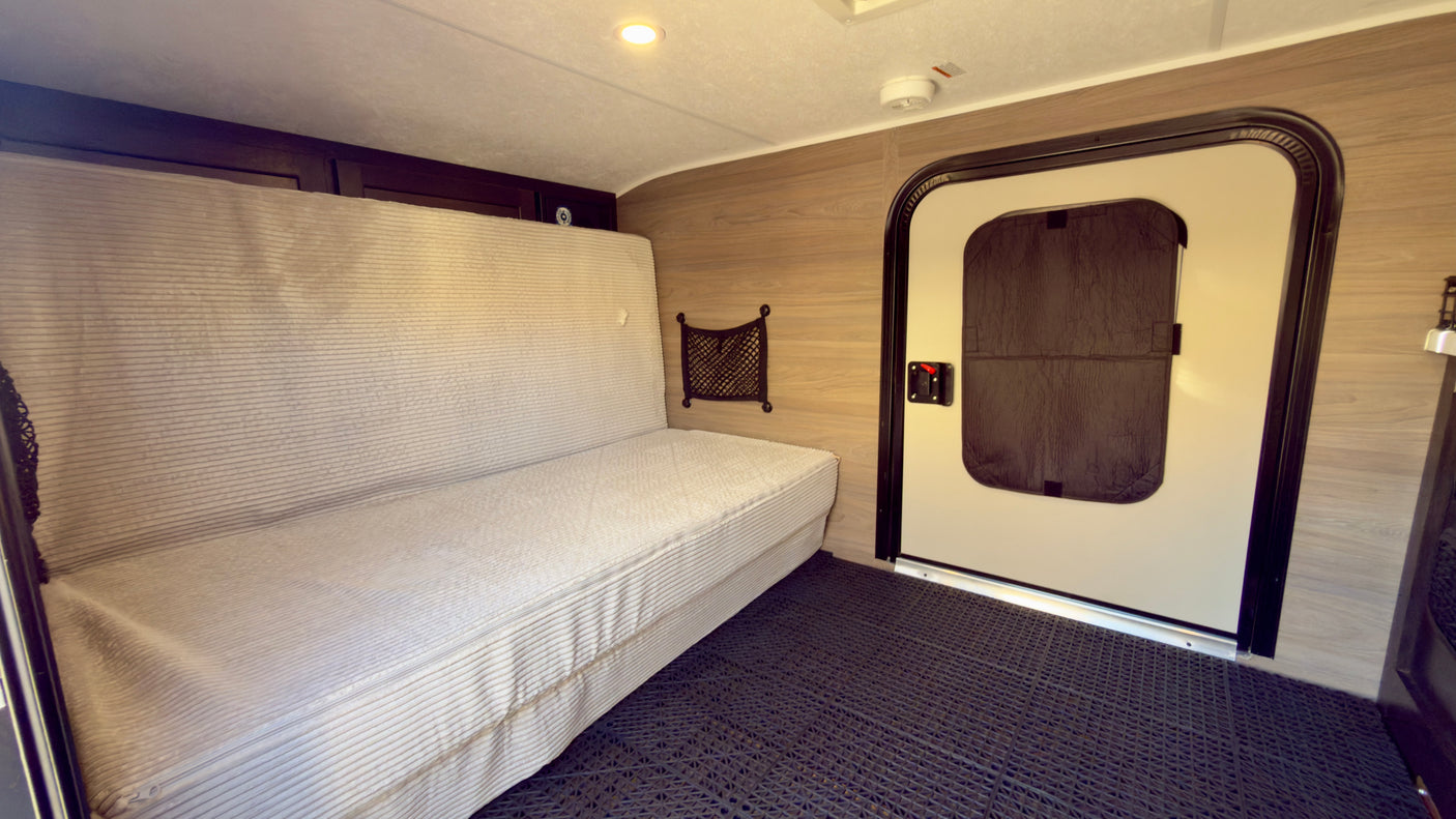 Inside an RV rental: a cozy sofa bed, entrance door, and textured floor. Perfect for compact living on the road.
