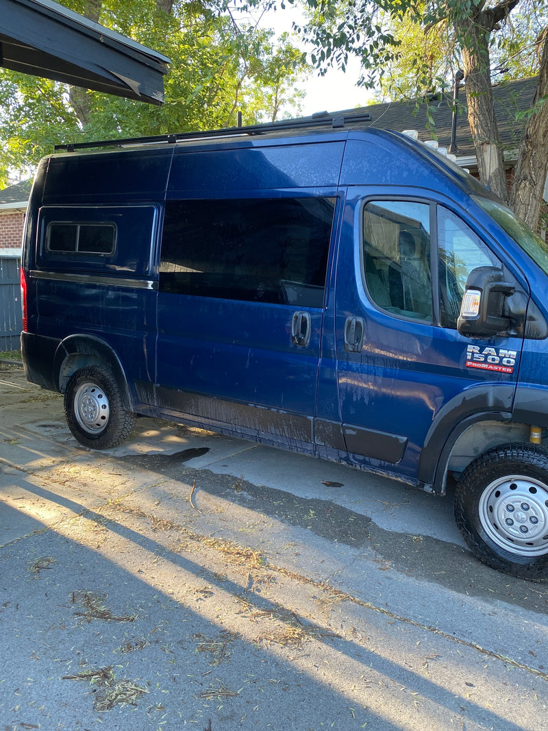 A blue Ram ProMaster camper van, ideal for RV rental, with a roof rack and customized windows, parked outside. — photo 11