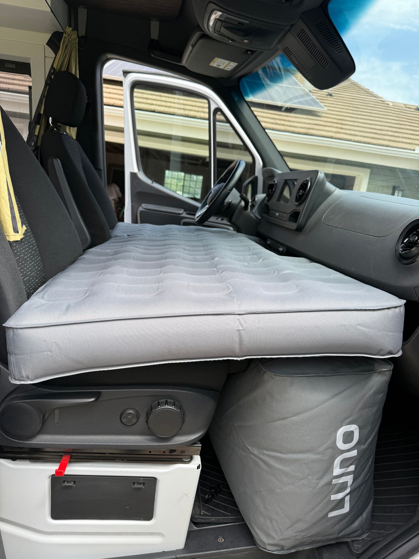 Inside an RV rental, a grey Luno air mattress spans the front seats, converting the cabin into a comfortable sleeping area.